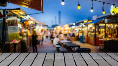 Image of wooden table in front of decorative outdoor string lights bulb in night market with blur people, Festival and holiday concepts, can used for display or montage your products.
